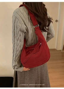 Detail of red crescent-shaped crossbody bag on a grey sweater for a minimalist retro look