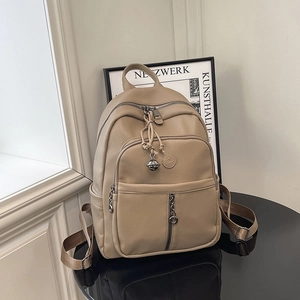 Detail eines beigen Rucksacks mit Lychee-Textur und silbernem Glockenanhänger