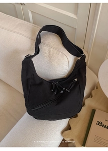 Detail of black canvas crescent bag with stylish diagonal zippers and tassel accents