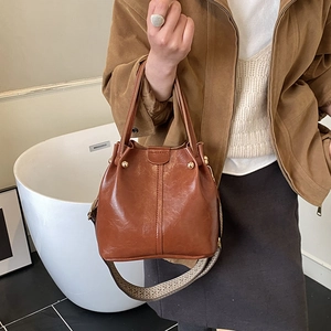 Brown bucket bag featuring gold metallic studs and a patterned woven wide strap