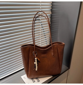 Détail du sac cabas en cuir marron foncé avec breloque en bois et éclairage latéral