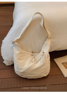Minimalist beige canvas hobo bag with zipper detail and matching strap on wooden floor
