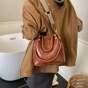 Detail view of brown leather bucket bag featuring a vintage jacquard wide shoulder strap
