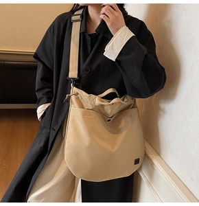 Close-up of khaki canvas crossbody bag featuring wide strap and small black logo label