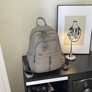 Detail eines grauen Rucksacks aus Leder mit Litschi-Struktur und Metallglocken-Anhänger