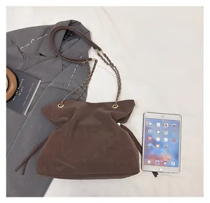 Detail view of large dark brown drawstring bucket bag with leather chain strap next to iPad