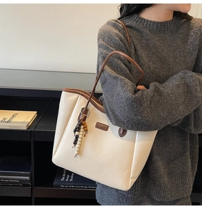 Détail du sac cabas crème minimaliste avec pendentif en perles de bois et étiquette en cuir