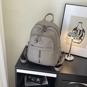 Grauer Rucksack aus genarbtem Leder mit Metallkette auf einem schwarzen Regal