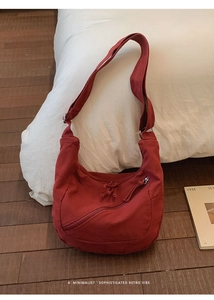 Detail of dark red canvas crescent bag with functional diagonal zipper and soft texture