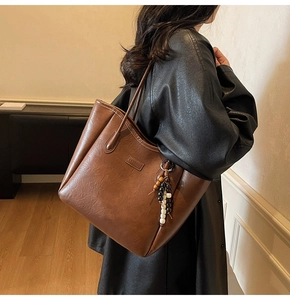Grand sac cabas marron avec breloque perlée porté par un mannequin en manteau