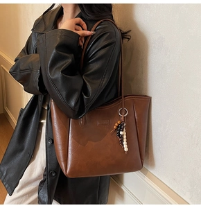 Détail macro du sac cabas en cuir marron avec logo embossé et pendentif en perles