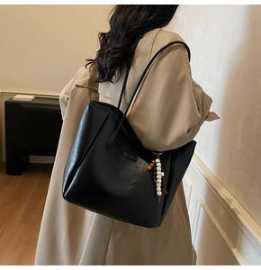 Détail du grand cabas noir en cuir grainé avec pompon en perles sur un trench-coat beige