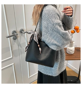 Detail of black pebbled leather bucket bag with decorative silk scarf and slim shoulder strap