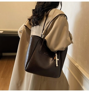Détail d'un sac cabas marron foncé avec pendentif en perles sur un trench-coat kaki
