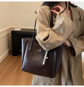 Détail du sac cabas en cuir marron foncé avec plaque en métal et pendentif perlé stylé