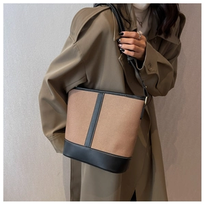Detail der Canvas-Eimertasche mit schwarzen Lederbesätzen und weißen Kontrastnähten am Modell