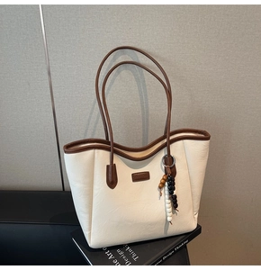 Détail d'un grand sac cabas beige avec bordure marron, écusson en cuir et pompon perlé