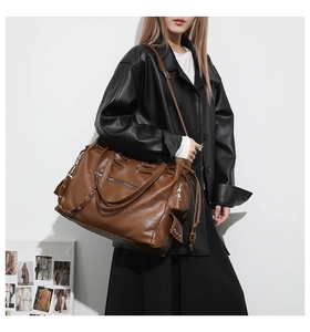 Detailed view of brown leather tote bag side pocket with metal zipper and rivet accents