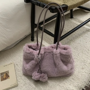 Gros plan d'un sac seau rose en fausse fourrure avec pompon assorti dans un décor cosy