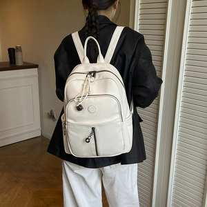 Detailansicht des cremeweißen Lederrucksacks mit mehreren Taschen und süßem Anhänger