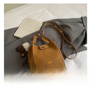 Braune Wildleder Beuteltasche mit Ziernaht und einem weißen Bommel Anhänger Detail