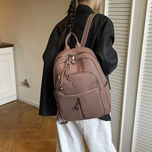 Detail eines staubrosafarbenen Rucksacks mit Lederstruktur und Metallglocken-Anhänger