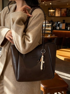 Grand sac cabas vintage en cuir marron avec charm perlé porté sur un manteau camel