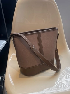 Braune Beuteltasche aus Canvas und Leder mit Kontrastnähten auf modernem Stuhl