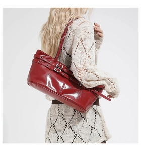 Deep red patent leather shoulder bag with buckle straps worn by a model in a casual outfit