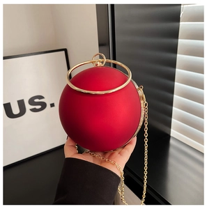 Macro view of a red spherical evening bag featuring a matte finish and gold ring handle