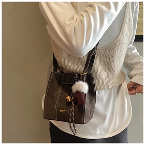 Close-up of brown suede bucket bag with white contrast stitching and festive charm