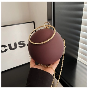 Detail view of a matte burgundy spherical evening bag with a golden ring handle and chain