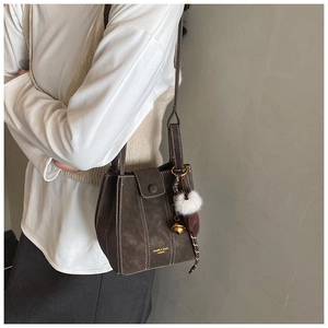 Detail of dark brown bucket bag with contrast stitching and decorative pom-pom charm