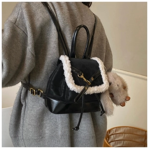 Detail of a black leather backpack with white faux fur trim and gold hardware on model