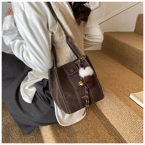 Detail of dark brown suede bucket bag with white stitching and fuzzy keychain accessory