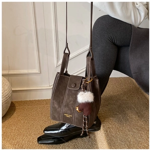 Detail of dark brown suede bucket bag featuring contrast stitching and plush charm