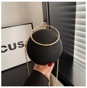 Detail of matte black spherical evening bag with golden circular handle and chain strap