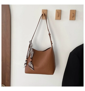 Detail of dark brown lychee leather bag with silk scarf on a wooden wall hook