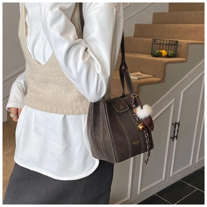 Close-up of dark brown suede bucket bag featuring contrast white stitching and fur ball charm