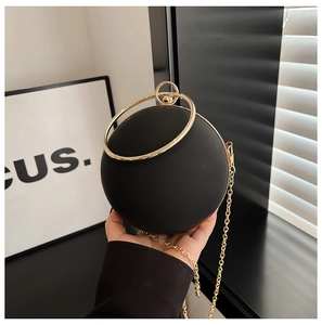 Detail of matte black spherical evening bag with golden ring handle and chain strap