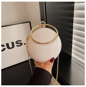 Detail of pearl white spherical evening bag with golden ring handle and chain strap