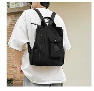 Detail of a black water-resistant backpack showing a side snap pocket and round logo patch