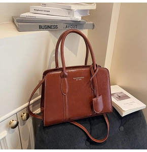 Detail of caramel brown faux leather handbag with embossed text and decorative pendant