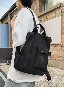 Side view of black nylon backpack with metal snap pocket on a brick wall background