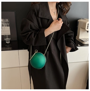 Detail of emerald green sphere bag with gold chain strap on a black trench coat