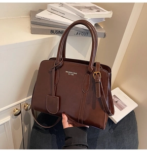 Close-up of golden MIKAXIQI logo on dark brown glossy patent leather handbag