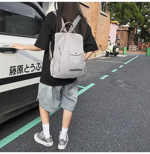 Outdoor street shot of a grey nylon backpack with vertical zippers and flap pocket