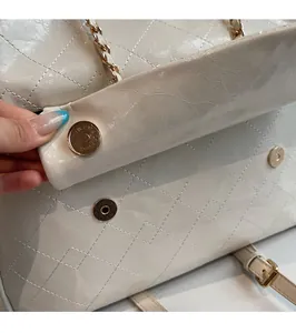Close-up of the magnetic buckle closure on a beige quilted patent leather shoulder bag