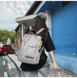 Outdoor view of a grey nylon backpack with multiple pockets and drawstring side details