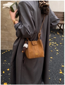 Detail of a brown suede bucket bag with white stitching and a plush charm in a street setting